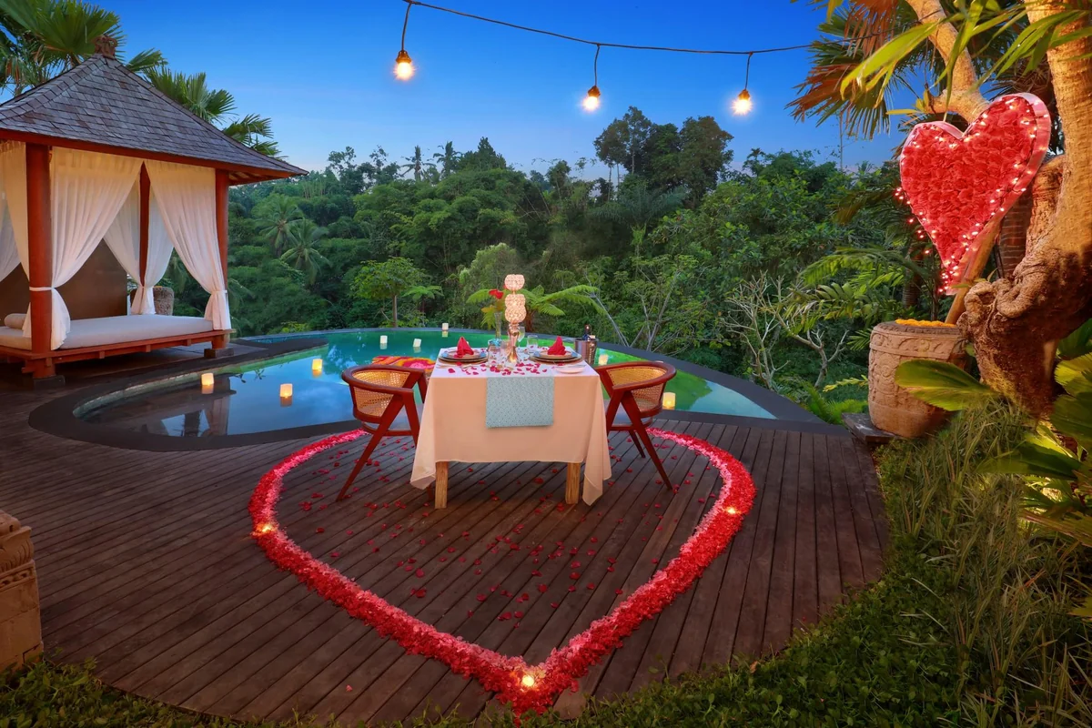Private dining table for two beside a tropical pool with rose petals and hanging lights