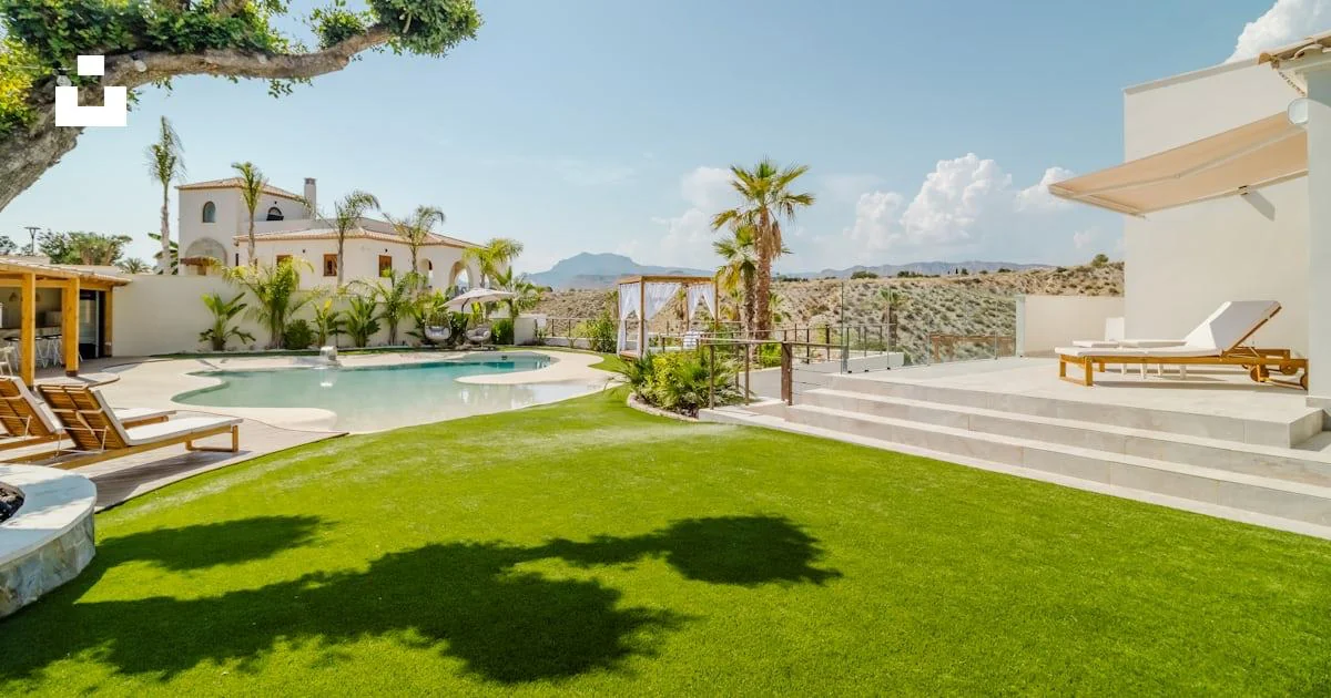 Villa garden with palm trees, a curved swimming pool and shaded loungers