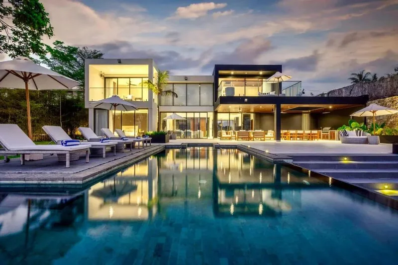 Illuminated modern villa with a swimming pool and sun loungers at dusk