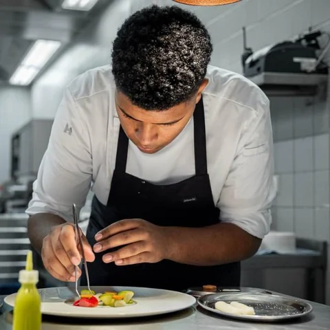 Chef carefully plating vegetables with tweezers in a professional kitchen