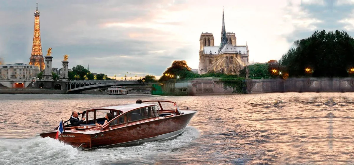 Wooden motorboat cruising along a city river past illuminated landmarks at dusk